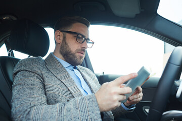 Mature bearded man using digital tablet he working online in the car