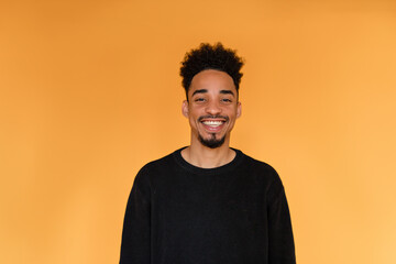 Studio portrait of afro american man wearing black pullover smiling over orange background. Portrait of dark-skinned cheerful man. Front view.