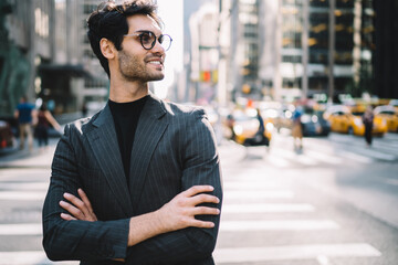 Side view of cheerful handsome man in stylish formal wear and spectacles looking away on Manhattan,...