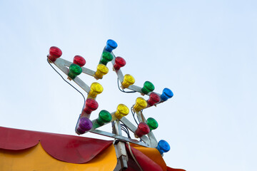 Star-shaped lamp with multi-colored light bulbs at top of circus or carousel. Illumination against sky background. Entertainment concept.