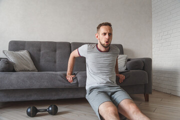 Young caucasian guy working out at home with sofa. Man doing physical excercises at home. Home work out fitness.