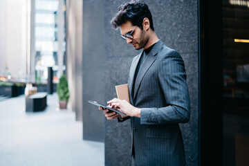 Pensive male entrepreneur holding portable pc outdoors checking income messages via 4g internet connection, young businessman browsing app on modern digital tablet reading latest news from website.