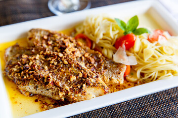 Pieces of fresh crispy breaded fish with noodle and vegetable served on plate. Top view, close up.