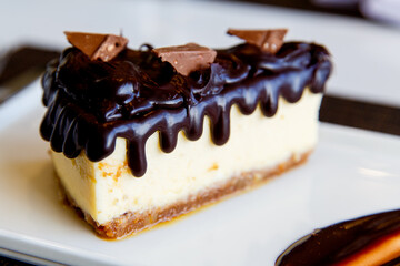 Cheesecake with chocolate sauce and pieces of chocolate served on a white plate. Close up. Tasty snack or coffee time with slice of cake.