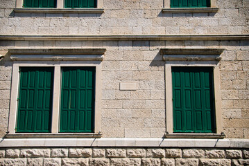 Fototapeta na wymiar Light stone wall of the house with the Windows shuttered