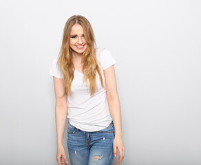 Obraz premium Pretty toothy laughing young woman with fair blond long hair in casual dress, blue jeans and t-shirt. Studio shot of good looking beautiful woman isolated against grey studio wall