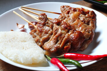 Thai sticky rice and juicy grilled pork or moo ping in Thai language are displayed on the wooden background