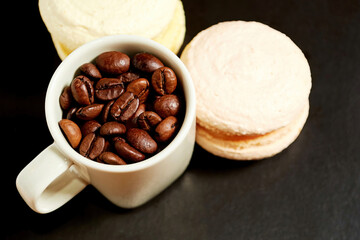 Espresso mug with coffee beans and two tasty macaroons on the black table surface. Food and drink backgrounds