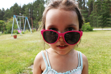 Little girl in beautiful pink sun glasses. A child in the summer in pink sunglasses.