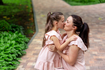 Happy mother and daughter 5-6 years old walk in the Park in the summer, mother kisses her daughter,...