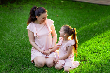 mother and daughter 5-6 years old walking in the Park in the summer, mother talking to her daughter sitting on the grass, the concept of a happy family, mother-child relations, mother's Day