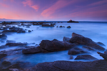Purple sunset over a rocky shore. A long exposure time has turned the waves into a misty blue haze 