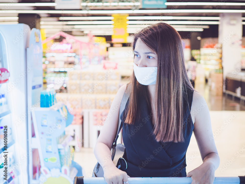 Wall mural asian woman wearing face mask shopping cart in supermarket department store during coronavirus crisi