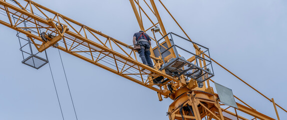 heavy equipment and crane mechanic with white helmet and harness repairing a crane with hand tools © JuanFrancisco