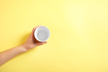 Disposable glass in hand on yellow background, top wiew.