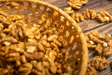 Peeled walnuts in a wicker basket and peeled walnuts scattered on a wooden table. Healthy diet. Fitness diet. Close up.