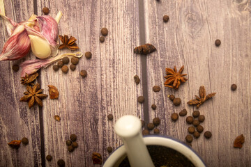 Allspice in a ceramic mortar and scattered garlic cloves, star anise and allspice on a wooden table. Close up.