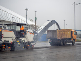 Cold milling machine loads crushed asphalt into a dump truck in cloudy weather