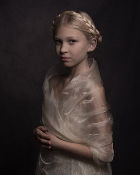 Portrait of beautiful blonde girl with classisc hair style and golden fabric around her shoulders in dark painterly rembrandt studio lighting