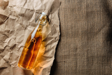 A bottle of homemade cider lies on kraft paper and burlap with copy space.
