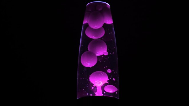 Retro lamp with bubbles. Concept. Beautiful colored bubbles rise and fall in neon lamp on black background. Lava lamp glows brightly in dark