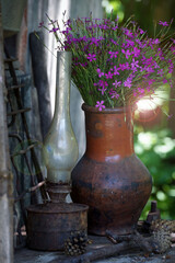 Still life in vintage style, a clay pot with flowers and an old rusty lamp on a shabby stand.