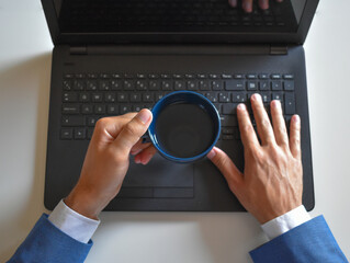Obraz na płótnie Canvas Man holding a cup of coffee while typing at the computer in the office