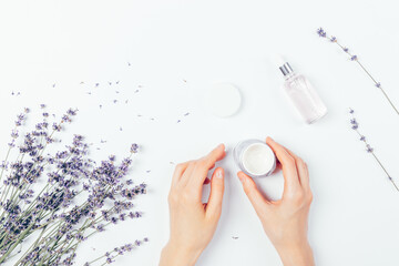 Female hands apply cosmetic cream next to bunch of lavender