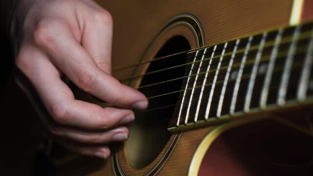 Close-up of man playing guitar. Concept. Professional guitar player moves fingers along strings of guitar beautifully. Atmospheric guitar playing