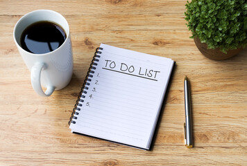 To do list written on notepad with pen, cup of coffee and flower on top of wooden table.