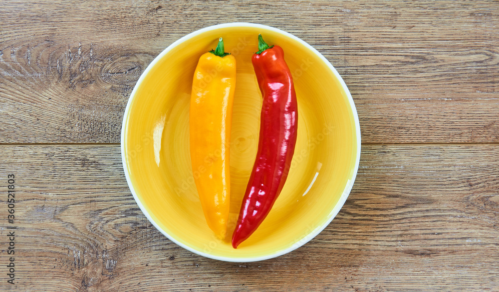 Wall mural yellow and red pods of sweet pepper on a yellow plate on a wooden tabletop