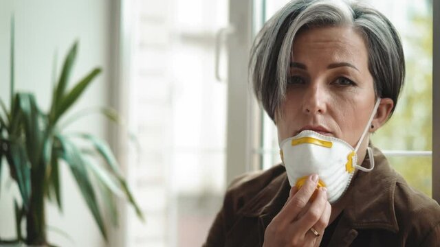mature woman with gray hair take off protection mask to have a free breath while sitting alone in the hallway leaned on the window. Business concept. Mature people in business. Prores 422.