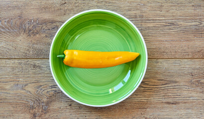 yellow pod of sweet pepper on a green plate on a wooden tabletop