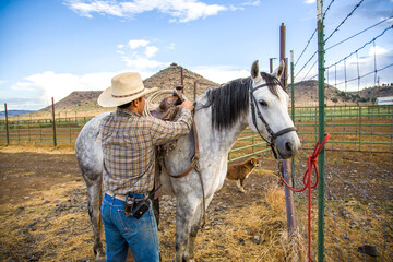 Paulina, Oregon, A cowboy placing a saddle on his horse on a ranch near Paulina, Oregon