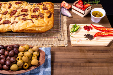 Fototapeta na wymiar Traditional Italian Focaccia with pepperoni, cherry tomatoes, black olives, rosemary ando onion - homemade flat bread focaccia