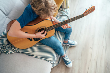 Top angle view at Preteen boy playing acoustic guitar dressed casual jeans, blue shirt sitting on...