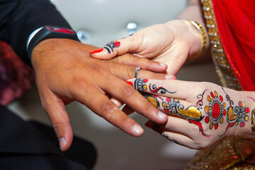 A bride is wearing a ring on the groom's finger. Indian Wedding.