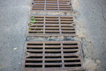 Rusty grating over the drainage channel. Cast-iron radiator grille for the storm sewer on the stone sidewalk.