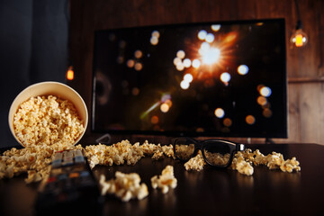 Craft bowl of popcorn on the dark table and TV remote control with TV set