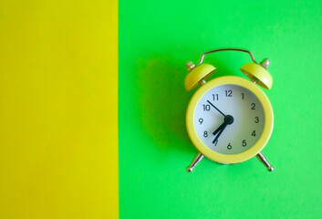 two-color yellow-green background, on the green part is a yellow alarm clock