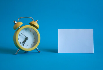 yellow alarm clock and blank white sheet on a blue background