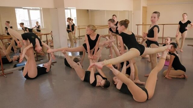 A group of young teenage girls in a ballet studio, they show a complex gymnastic exercise. Various gymnastic and dance support performed by young ballerinas. Group ballerinas dance at a ballet school.