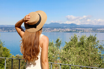 Beautiful tourist woman with hat enjoying view of Lake Garda from stunning village of Sirmione, Italy