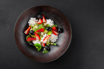 Plate with fruit salad, kiwi, strawberries, blueberries, apple, whipped cream