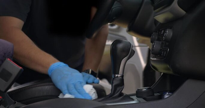 A man wearing blue rubber gloves cleans and sanitizes a car's interior before sale or after a test drive. Extra cleaning was a common sight during the coronavirus COVID19 pandemic of 2020.  	