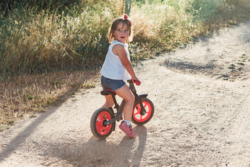 Blond hair girl riding a bicycle on a dirt road