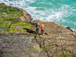People fishing off the rocks at Murawai Beach, Auckland, New Zealand