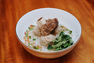 meatball soup with vermicelli and beef ribs. indonesian street food. white bowl. pieces of mustard leaf