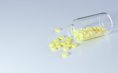 Yellow pills in the glass bottle on the white table