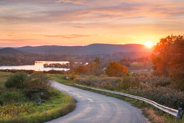 sunset over the road with a beautiful lake and autumn foliage in the background